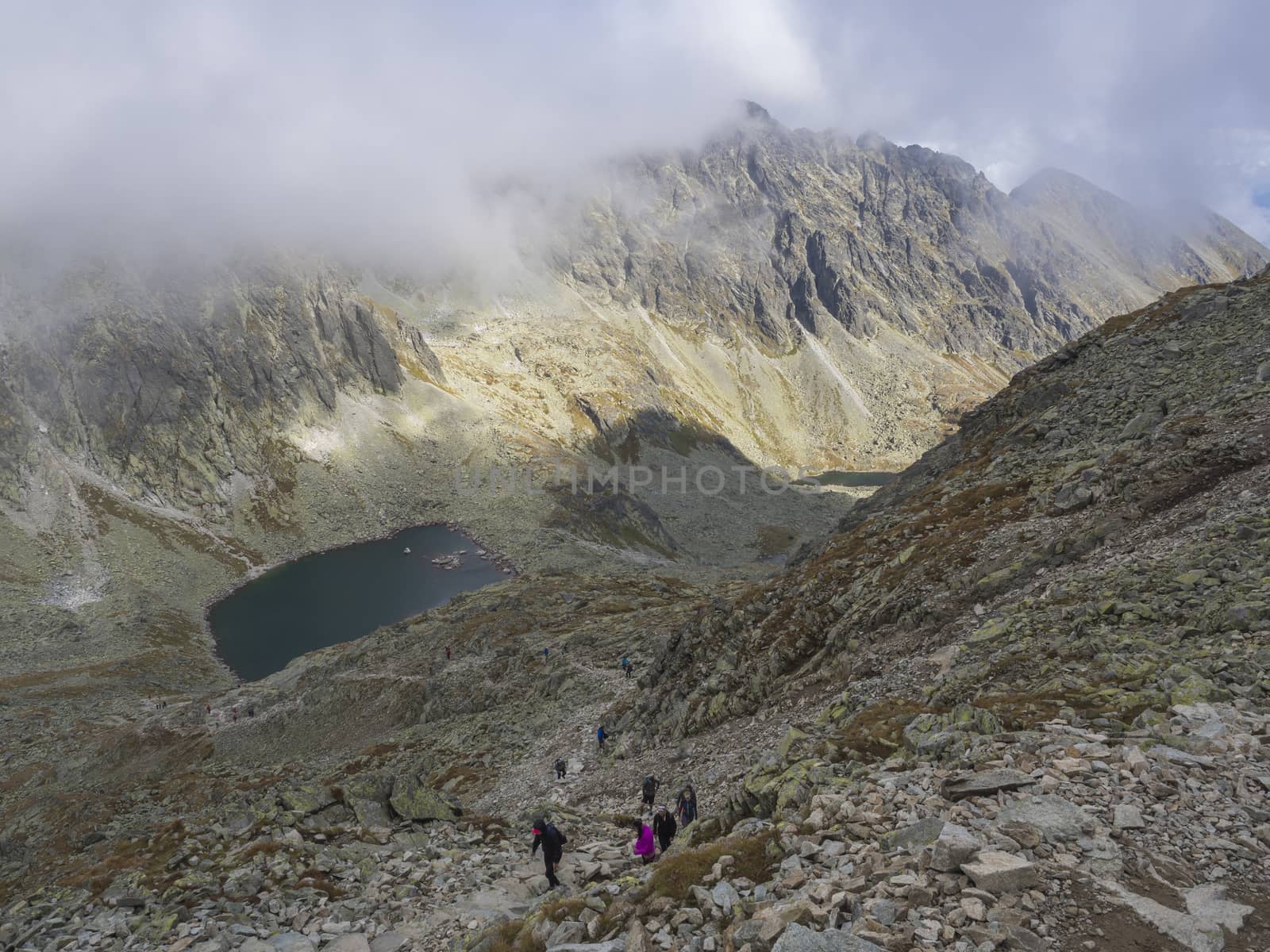 Panorama from Bystra lavka 2300m with the mountain lake Capie and Okruhle pleso with hikers climbing up, Mlynicka dolina and peak Strbsky stit 2381m , slovakian high Tatra mountains. fog and dramatic light.
