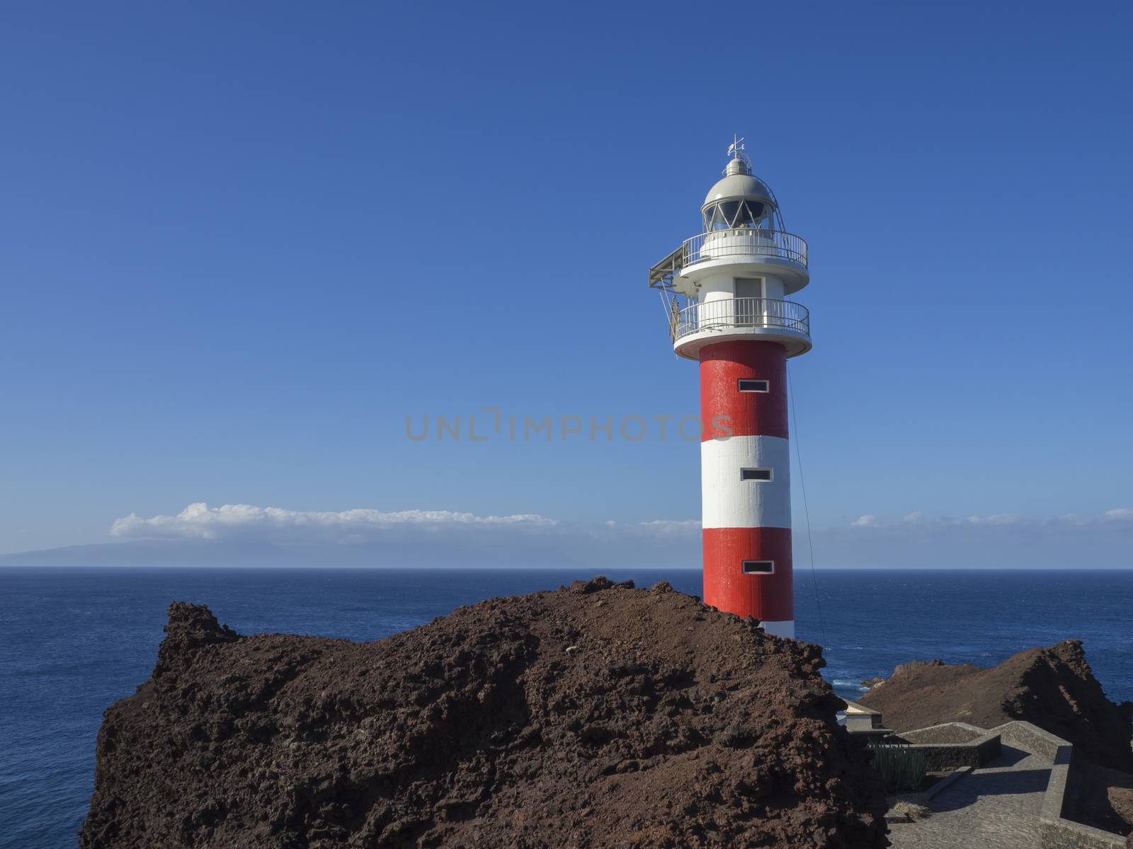view on red white lighthouse on Punta de Teno cape on west Tenerife canary island with lava rock blue sea and clear summer sky