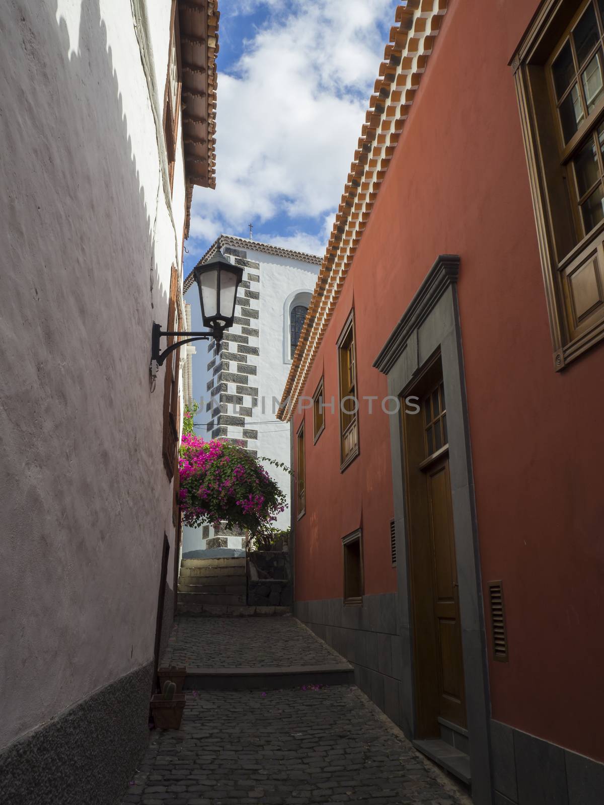 narrow street in old village garachico with traditional red and white houses latern flowers and blue sky by Henkeova