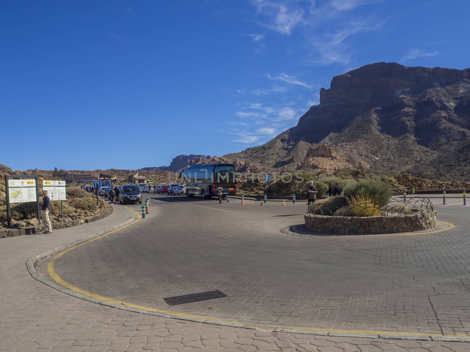 Spain, Canary islands,Tenerife, El Teide national park, December 21, 2017, traffic circle on parking at Roque Cinchado famous pitoresque rock formation Roques de Garcia with group of tourist, bus, parked cars, touristic notice and blue sky background