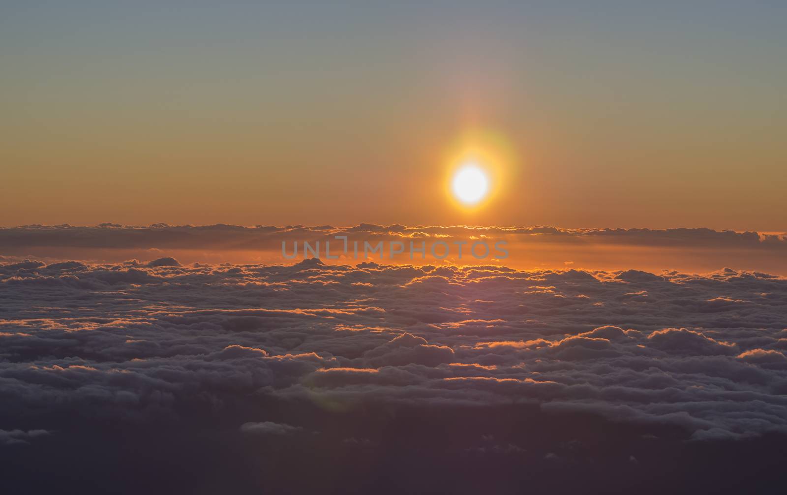 orange red sunrise, sun rising above the fluffy clouds with sunbeam rays and lens flare, taken from top of pico del teide tenerife