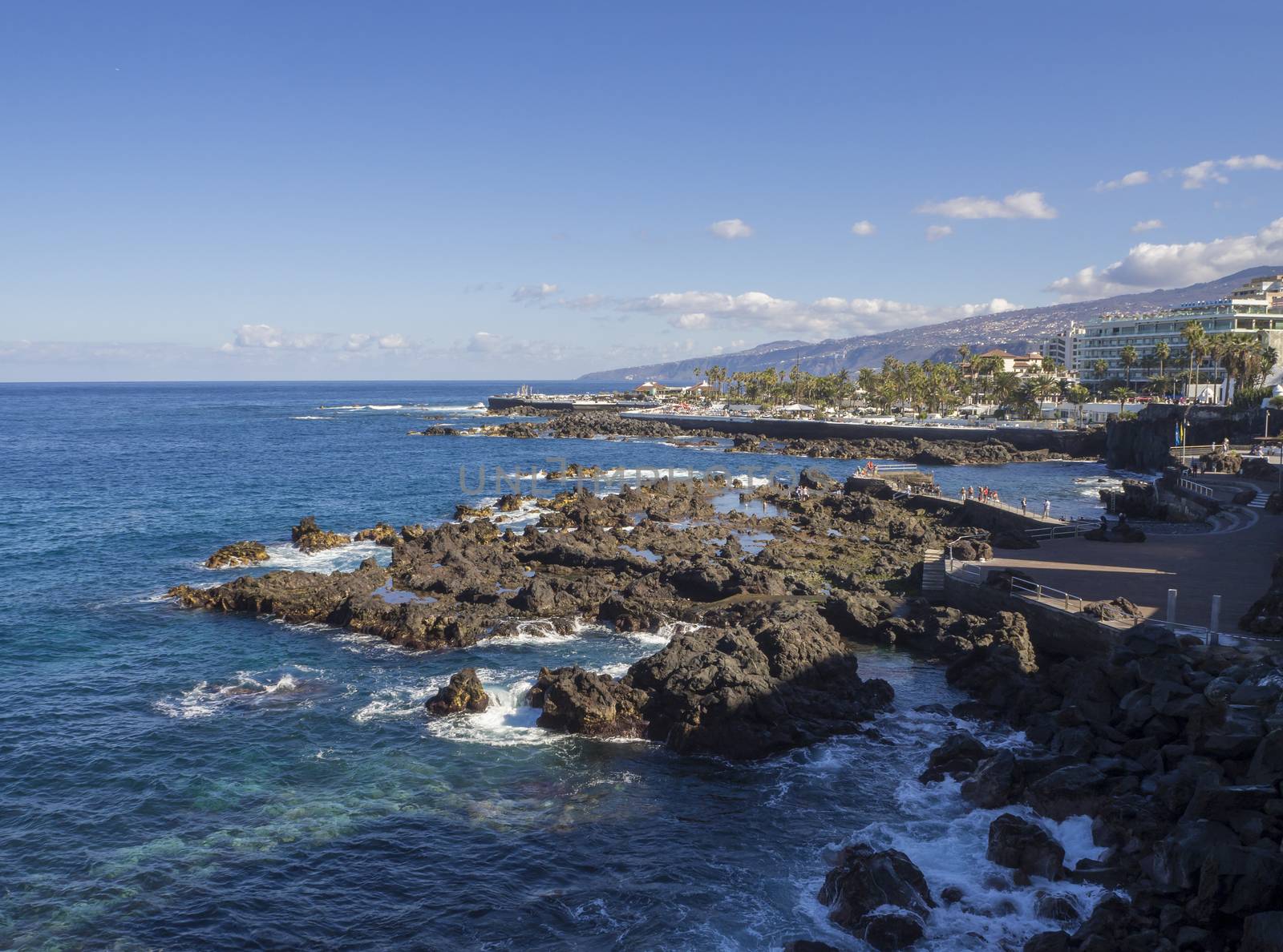 Spain, Canary islands, Tenerife, Puerto de la cruz, December 23, 2017, view on rocky sea pool with big hotel resort buildings panorama of Puerto de la cruz, tenerife with green hill and blue sky background