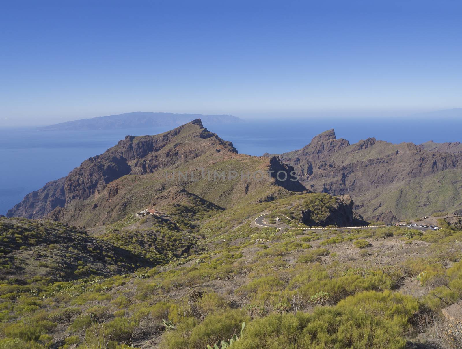 view on asfalt road to village Masca in Tenerife with green hills, sharp mountain peaks, sea horizon and clear blue sky background