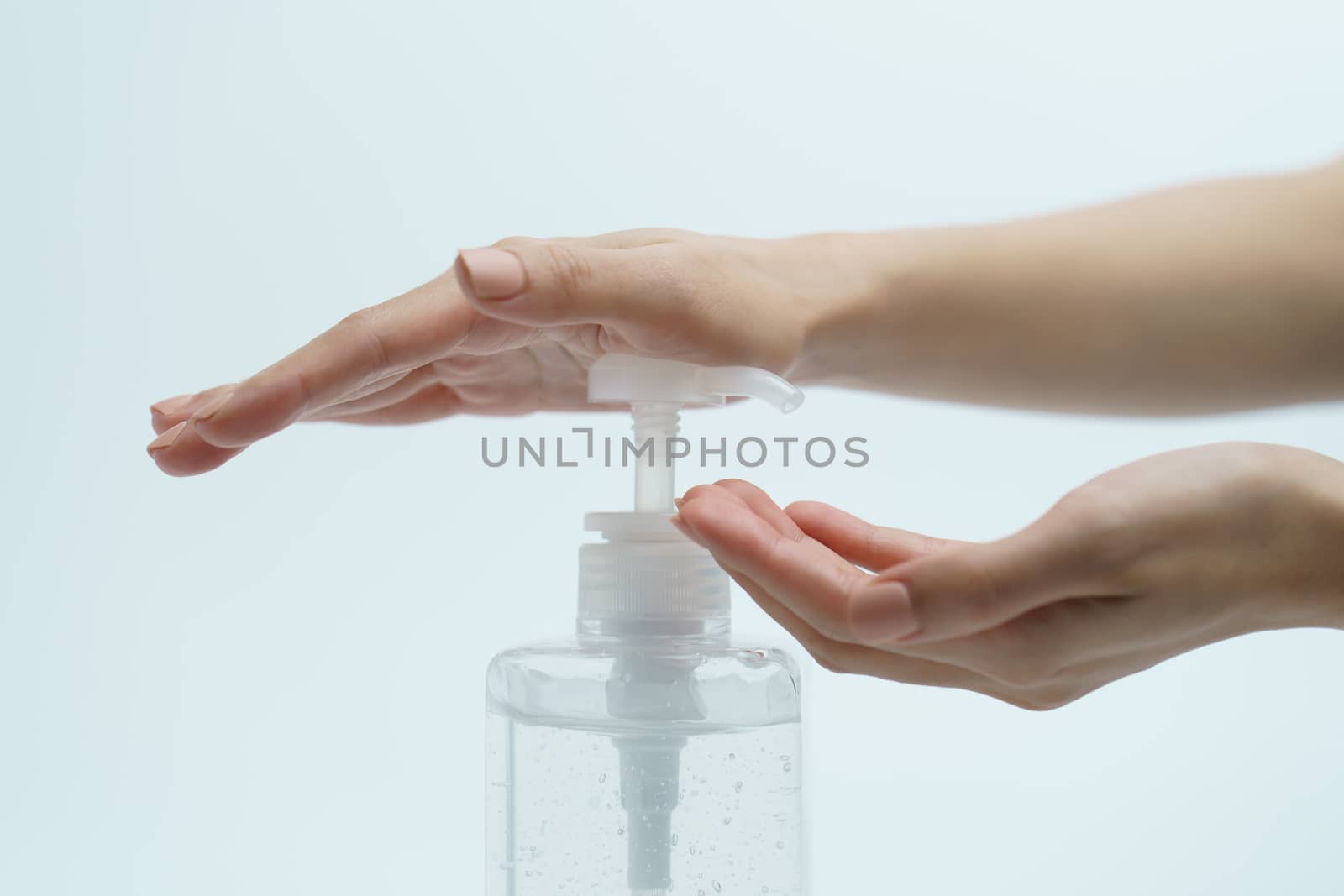 Hand with hand sanitizer in a clear pump bottle on a white background.