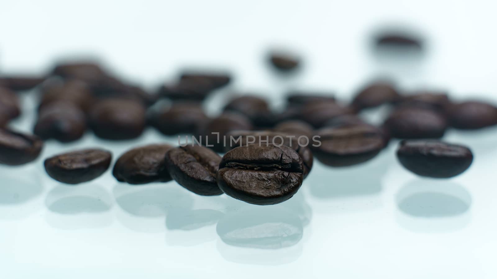 Roasted coffee beans pile on white glass reflection background