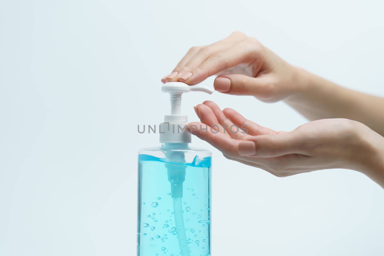 Hand with hand sanitizer in a clear pump bottle on a white background.