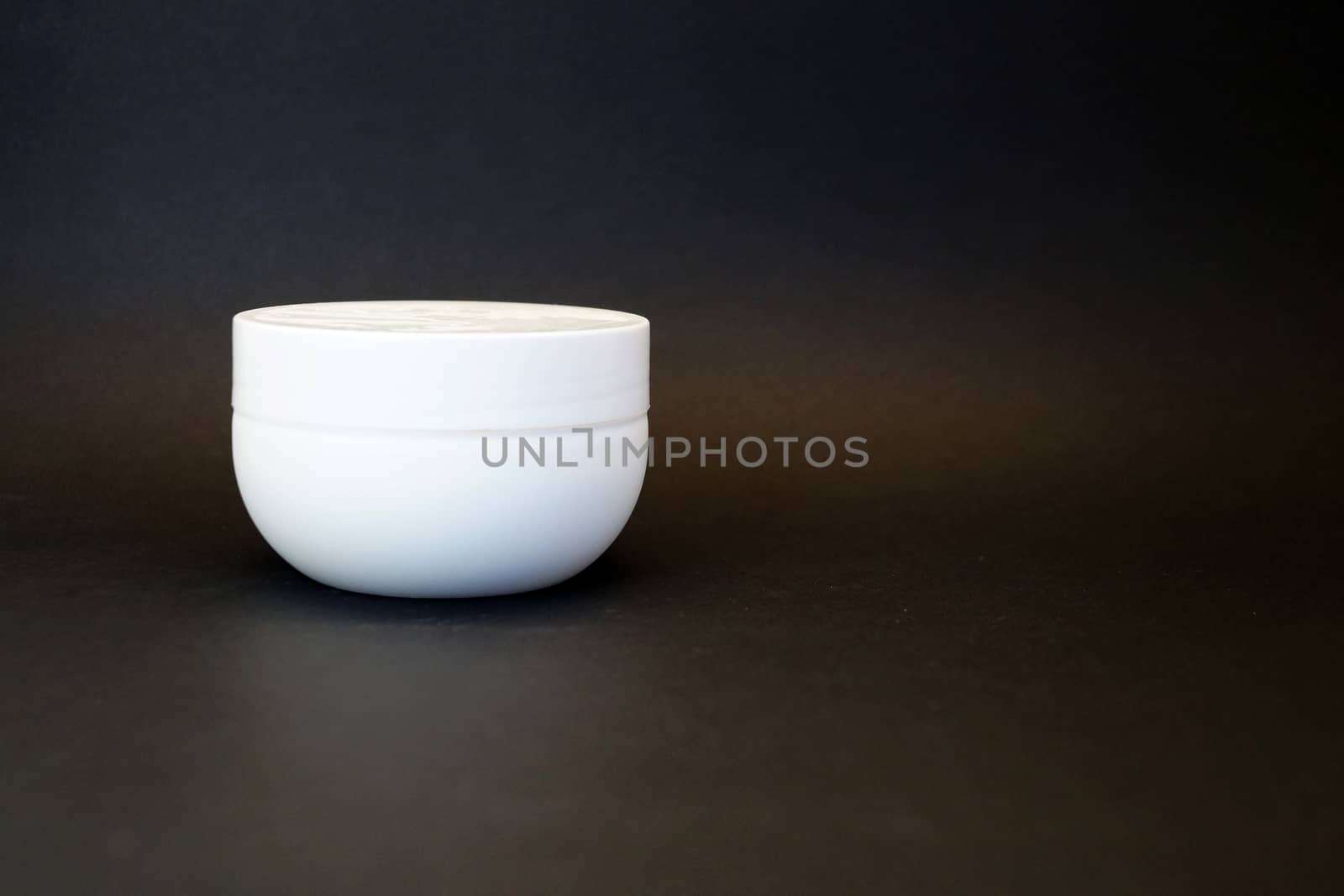 white cream jar on black background close up, copy space