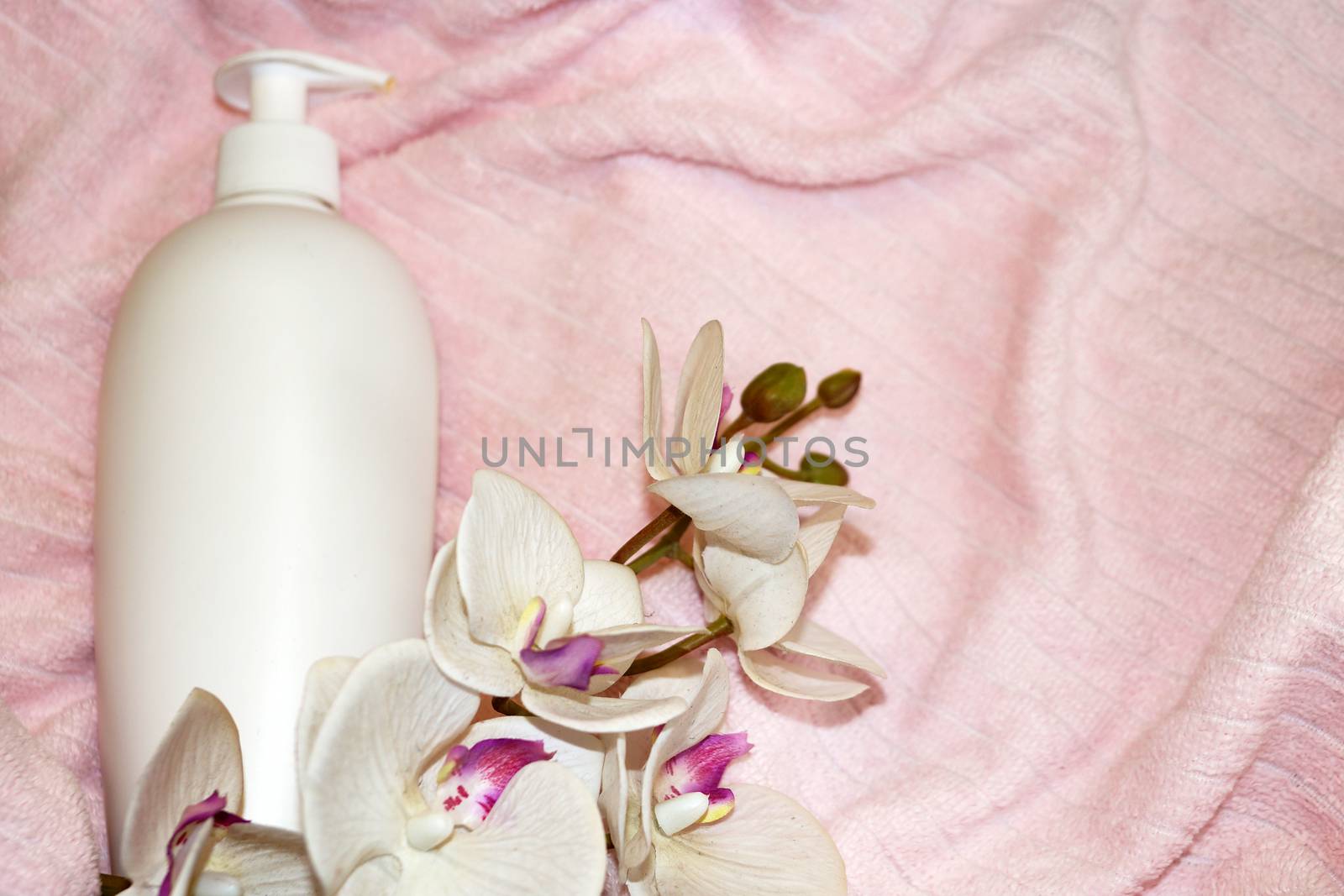 white cosmetic bottle and white orchid flower on pink terry cloth close up