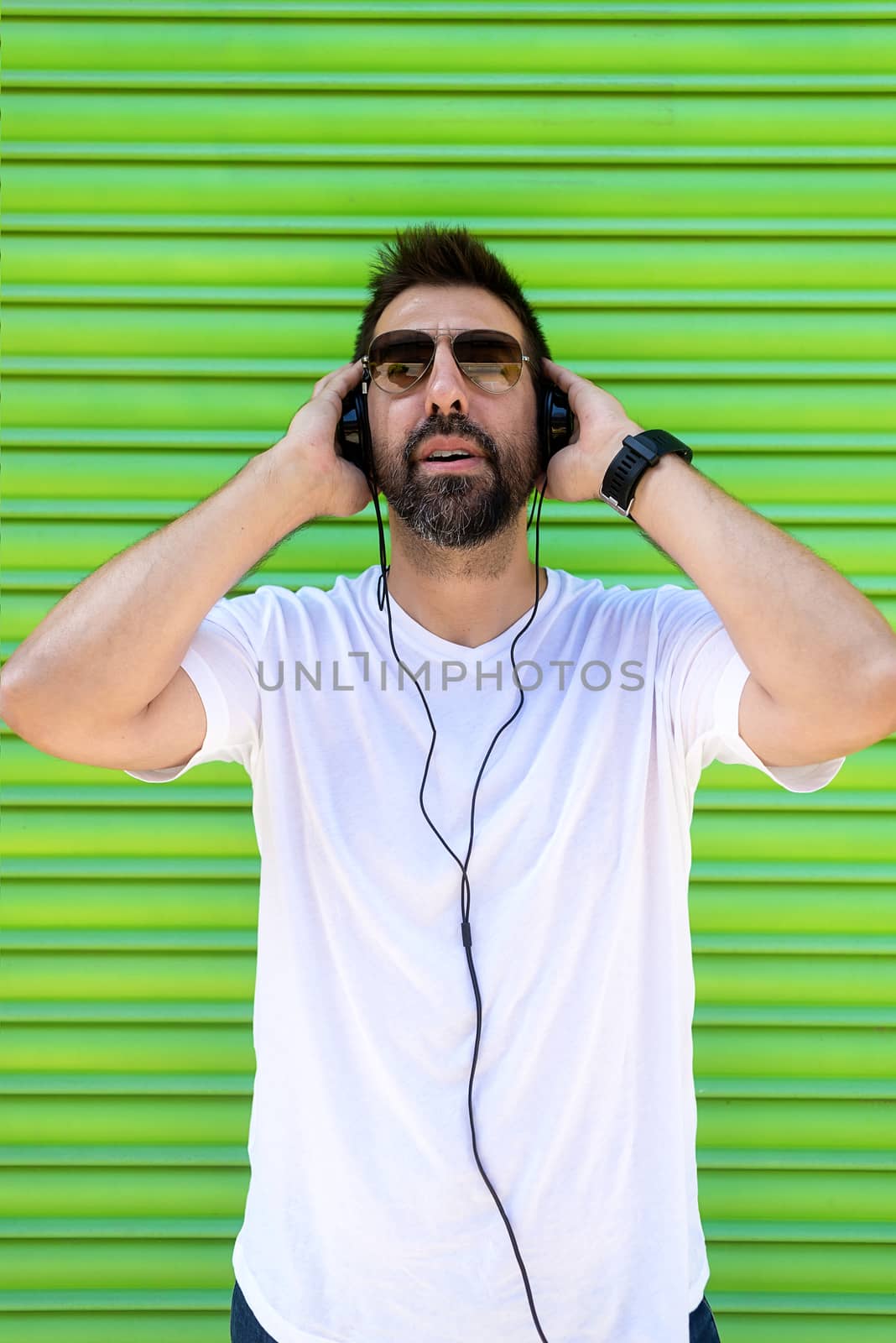 Cool trendy funny beard guy in headphones listening music on colored background.