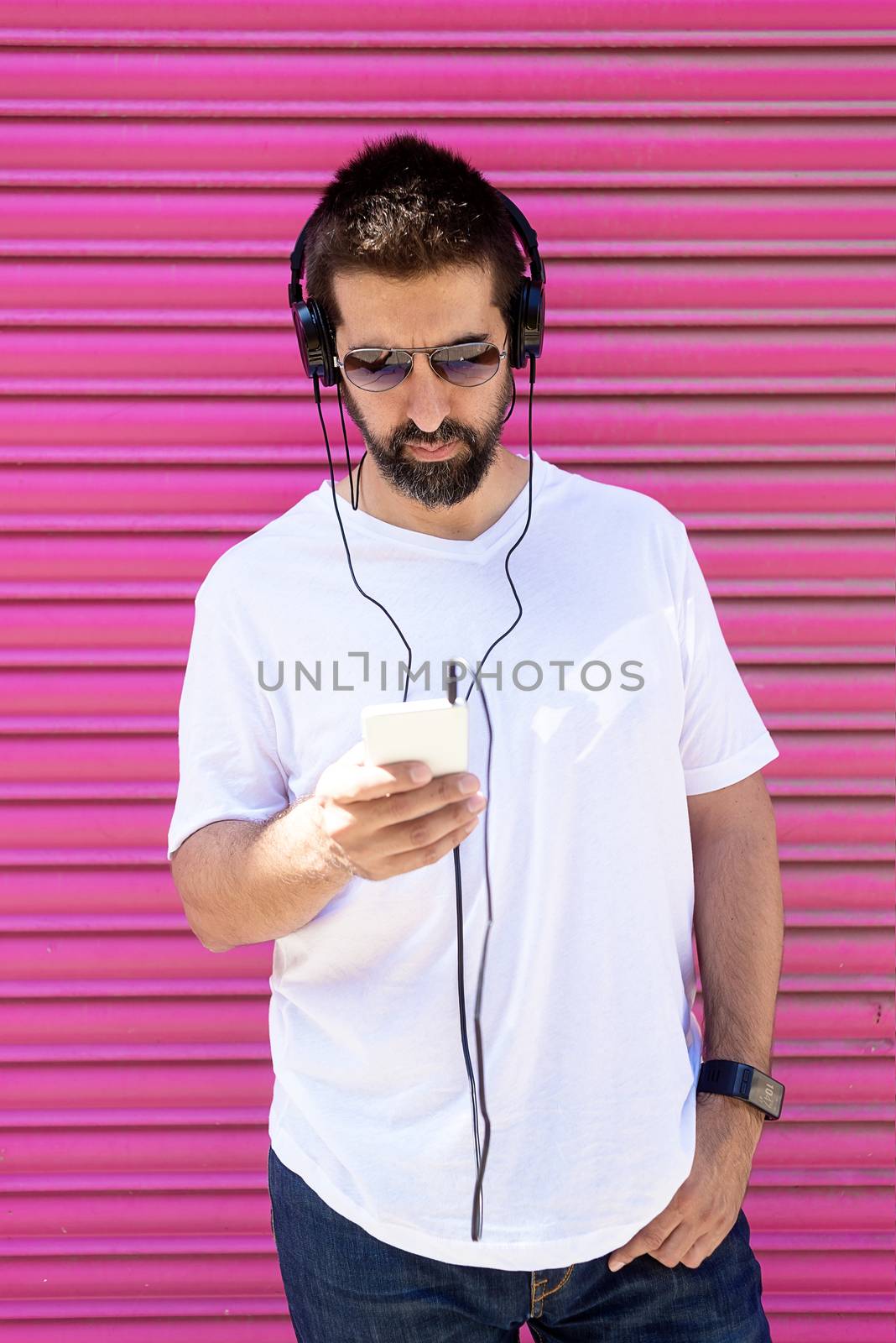 Bearded man with headphones and sunglasses using a smartphone while listening music by raferto1973