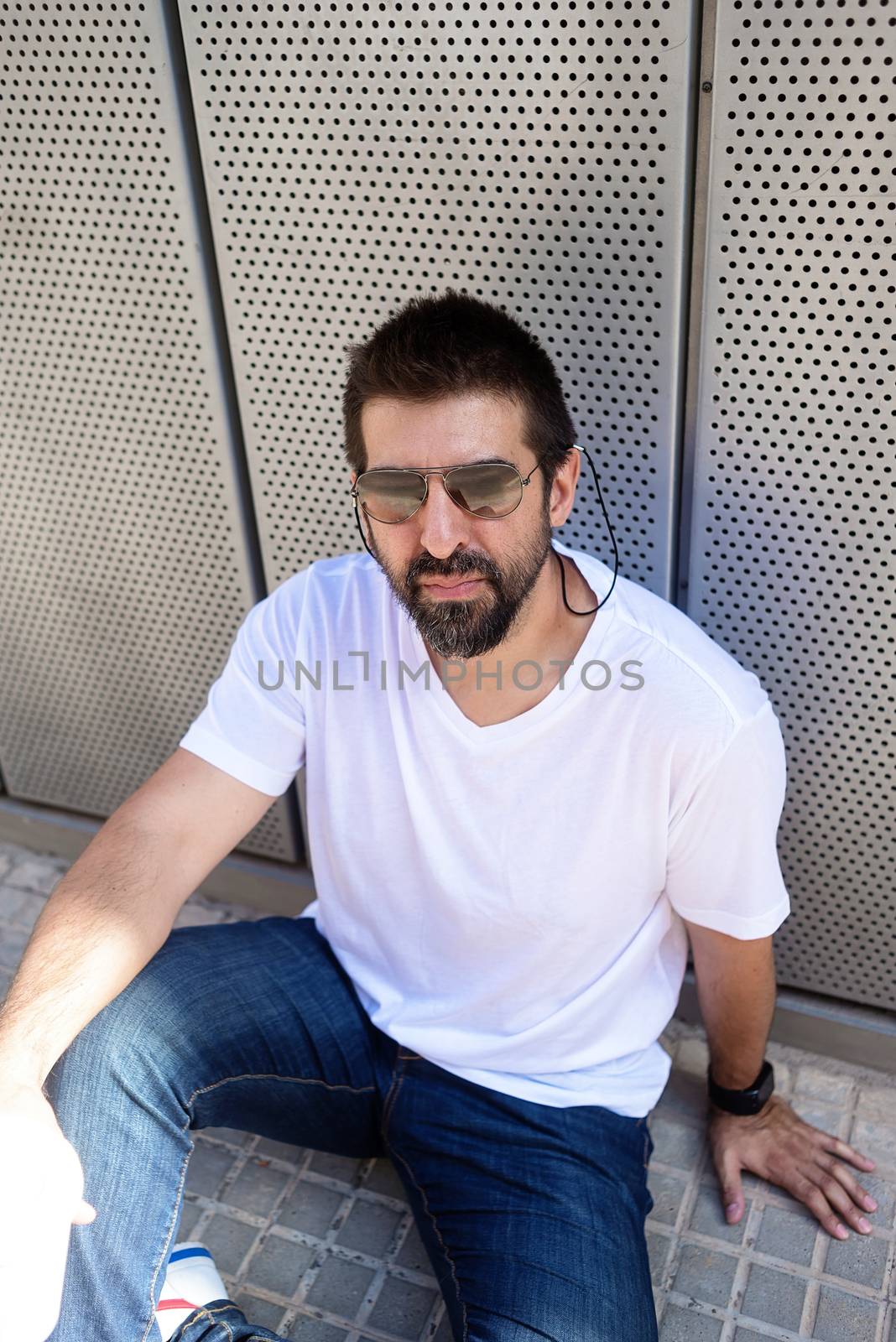 Bearded guy with sunglasses sitting on ground outdoors