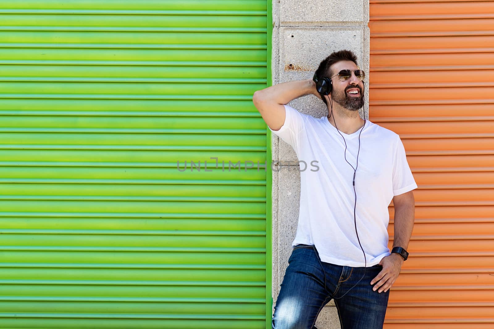 Cool trendy funny beard guy in headphones listening music on colored background.