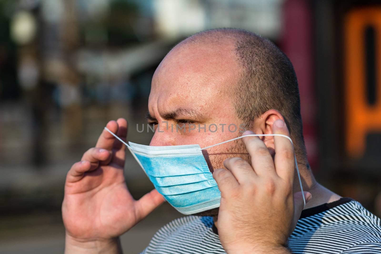 Young man with medical protective face mask illustrates pandemic coronavirus disease on blurred background. SARS-CoV-2 outbreak in Europe. Changes and complications caused by epidemic