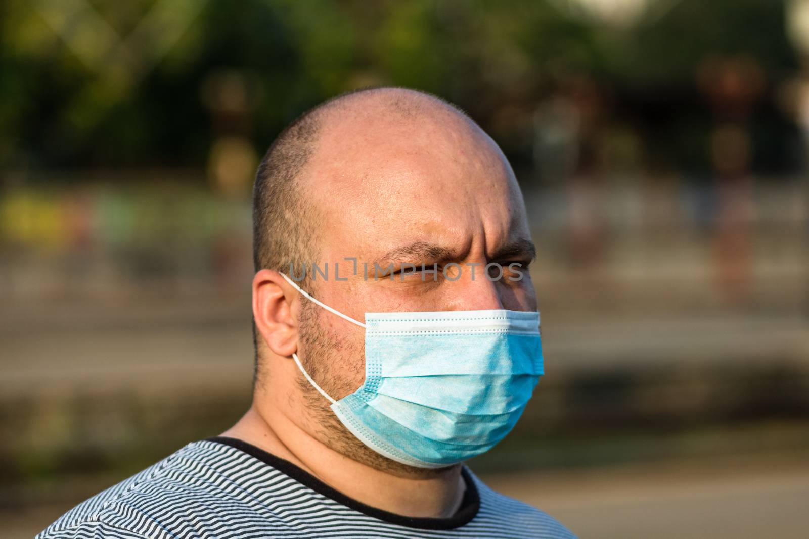 Young man with medical protective face mask illustrates pandemic coronavirus disease on blurred background. SARS-CoV-2 outbreak in Europe. Changes and complications caused by epidemic