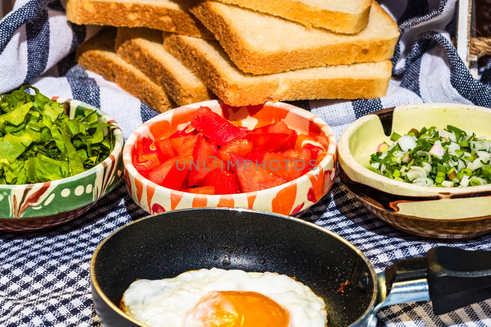 Close up of fried egg in a small frying pan  and different bowls with copped vegetables in a rustic composition