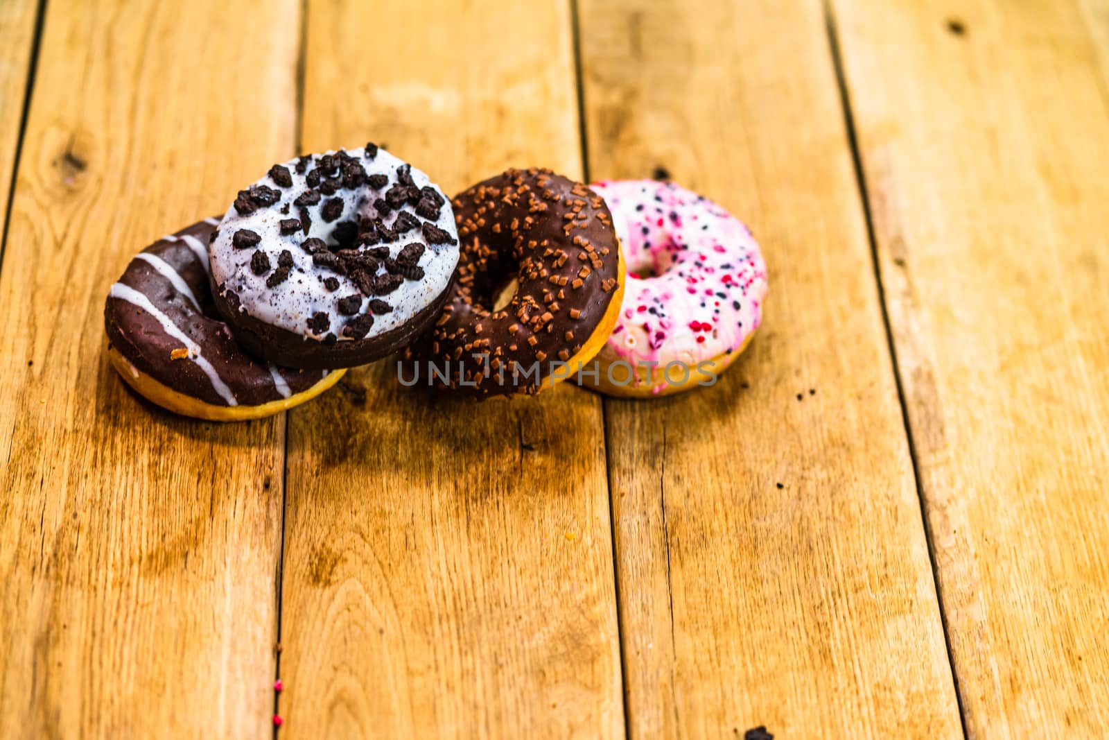 Colorful donuts on wooden table. Sweet icing sugar food with glazed sprinkles, doughnut with chocolate frosting. Top view with copy space