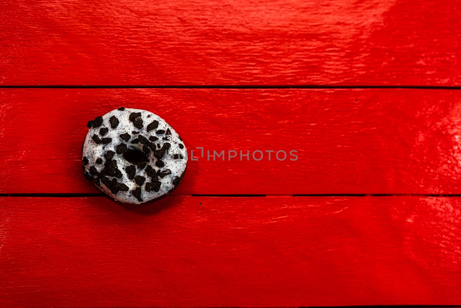 Colorful donuts on red wooden table. Sweet icing sugar food with glazed sprinkles, doughnut with chocolate frosting. Top view with copy space