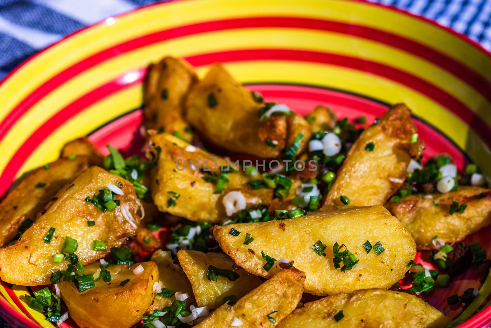 Close up with selective focus of fried potatoes with green onion, green garlic and spices in a colorful plate.