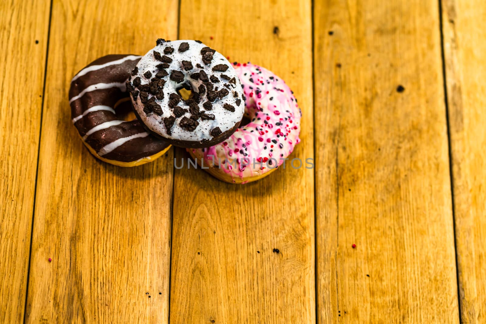 Colorful donuts on wooden table. Sweet icing sugar food with glazed sprinkles, doughnut with chocolate frosting. Top view with copy space