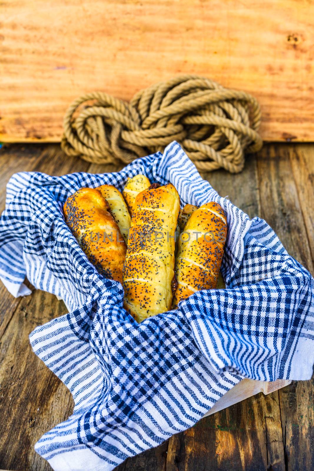 Sausages baked in dough sprinkled with salt and poppy seeds in a rustic basket. Sausages rolls, delicious homemade pastries in a rustic composition.