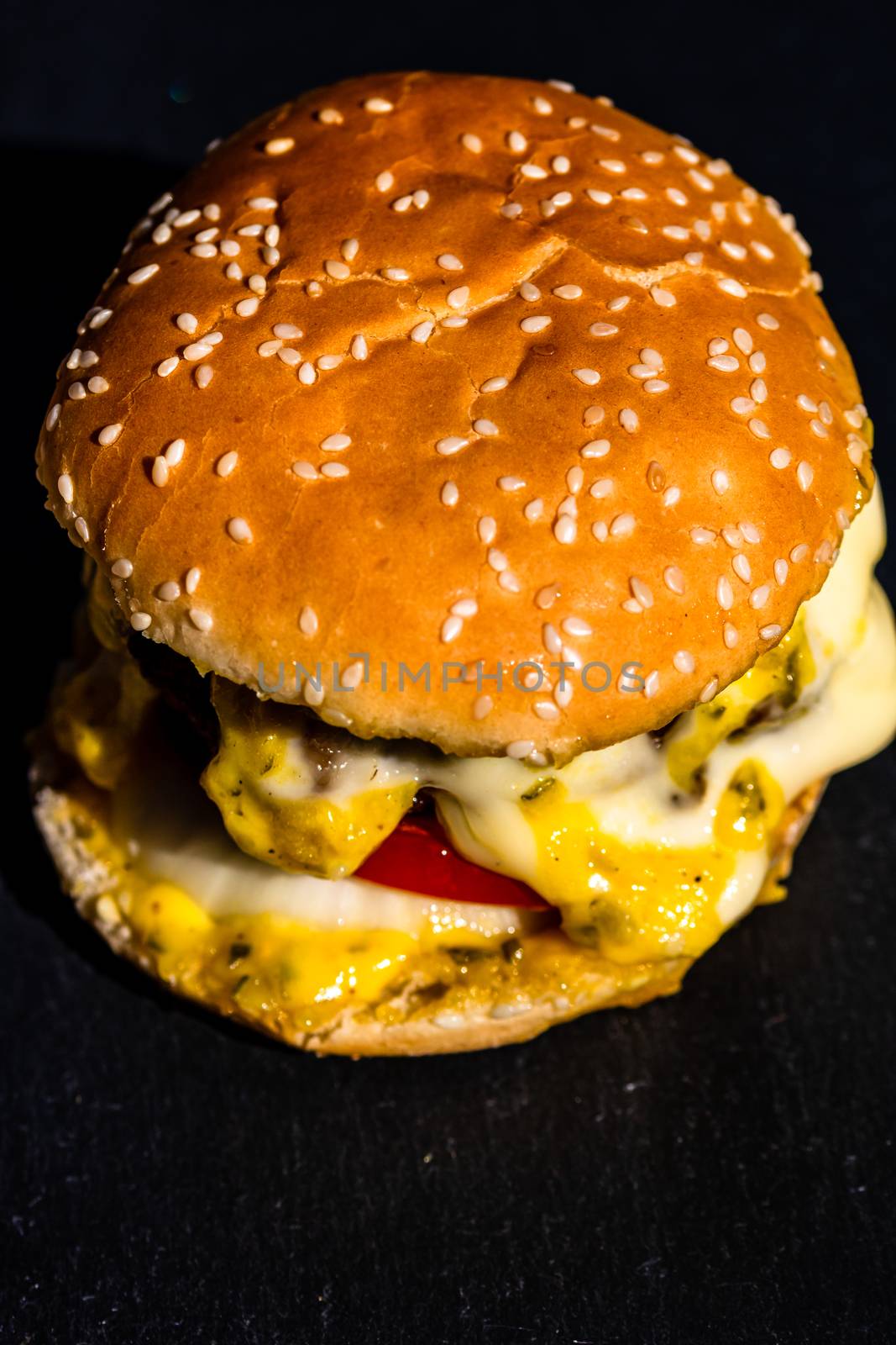 Detail of beef cheeseburger with melted cheese isolated on black by vladispas