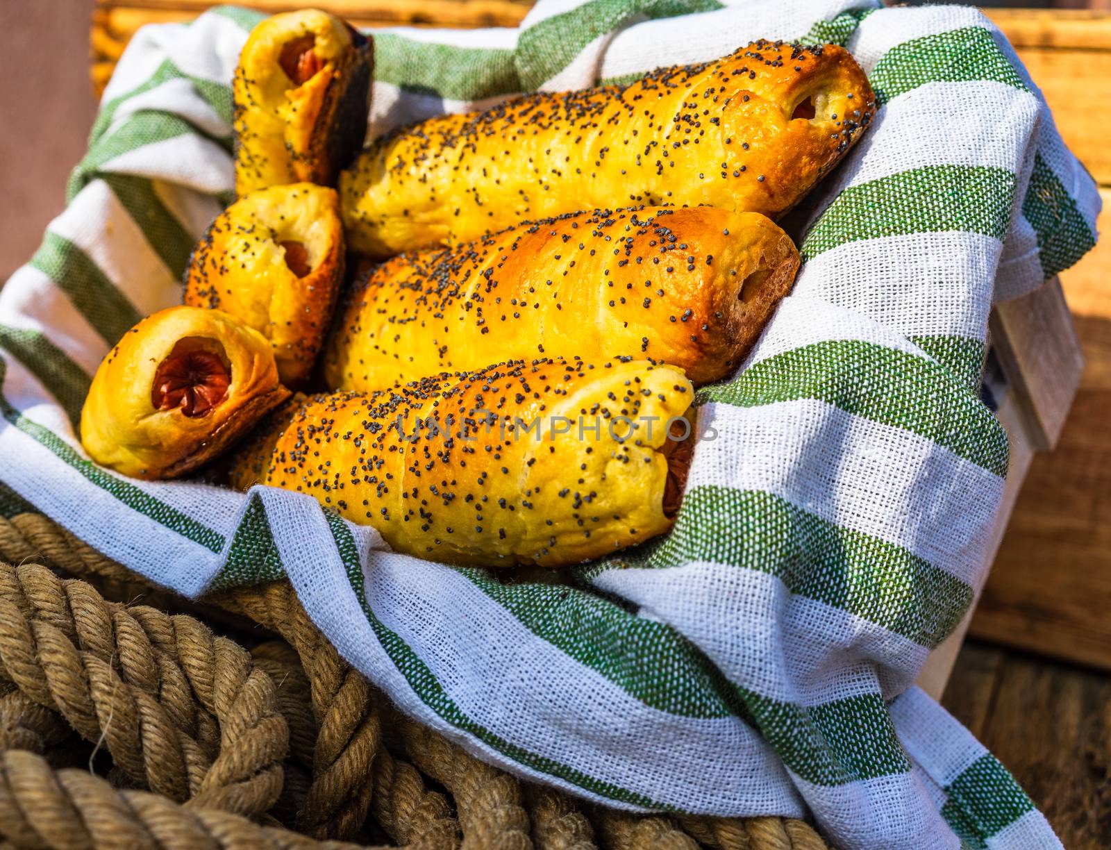 Sausages baked in dough sprinkled with salt and poppy seeds in a rustic basket. Sausages rolls, delicious homemade pastries in a rustic composition.