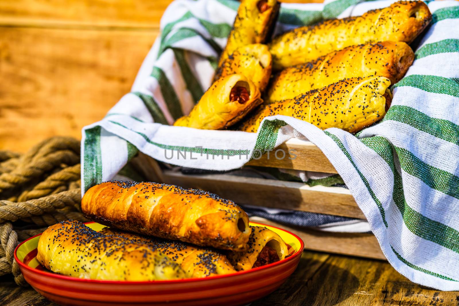 Sausages baked in dough sprinkled with salt and poppy seeds in a rustic composition. Sausages rolls, delicious homemade pastries.