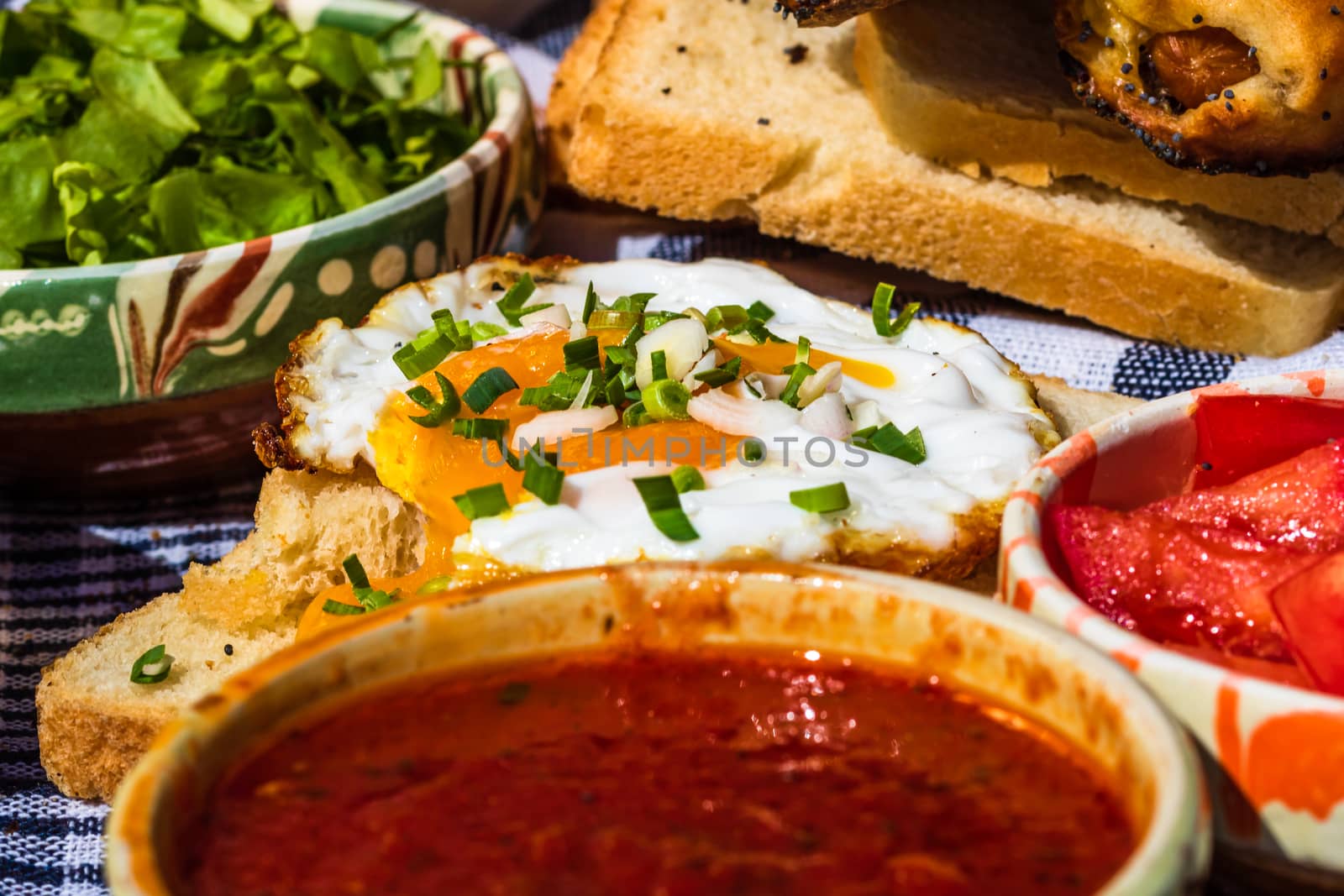 Rustic composition with sausages rolls, fried egg on toast bread, different bowls with sauce and chopped vegetables.