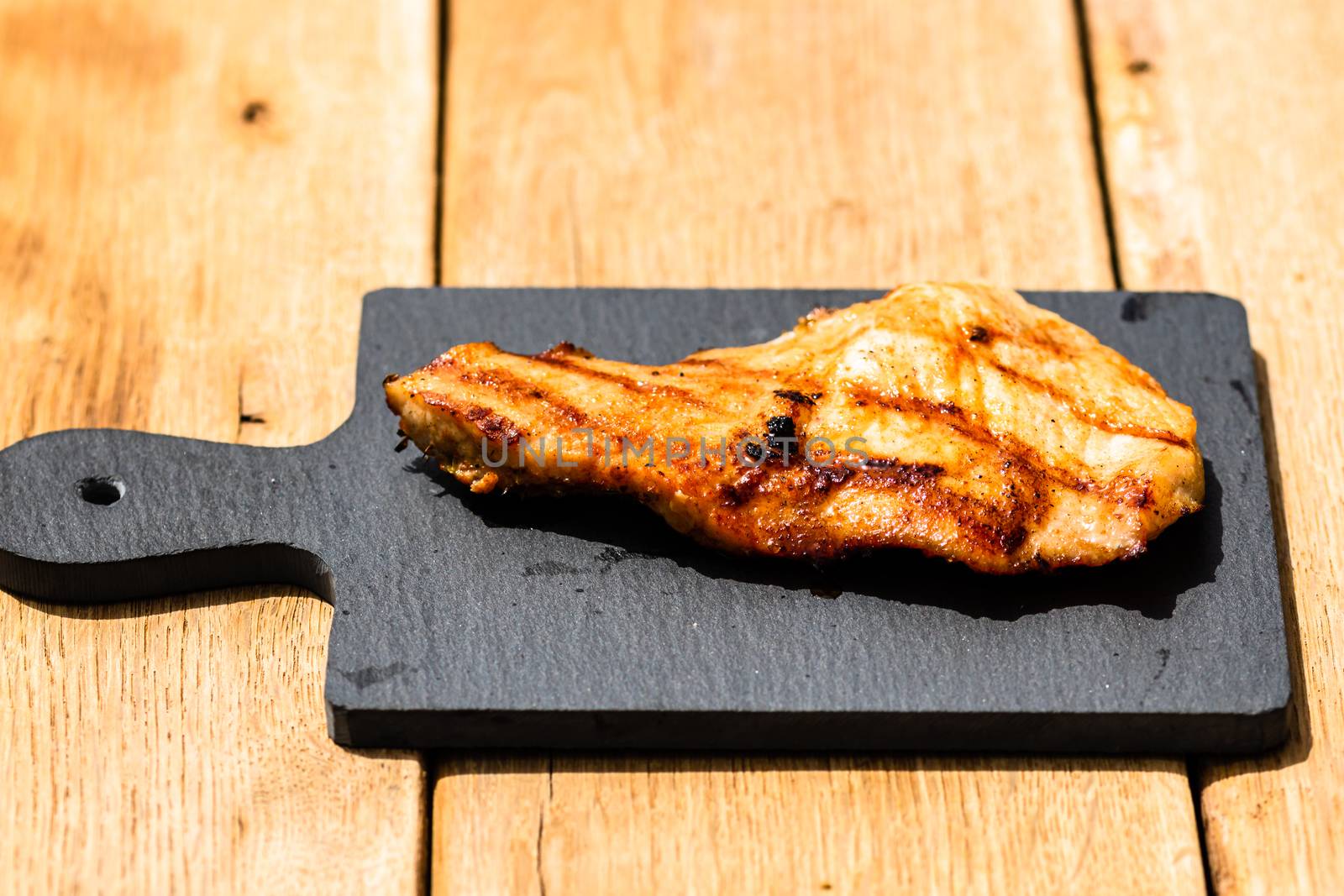 Close up of grilled steak on small black chopping board isolated. Barbecue, grill and food concept.