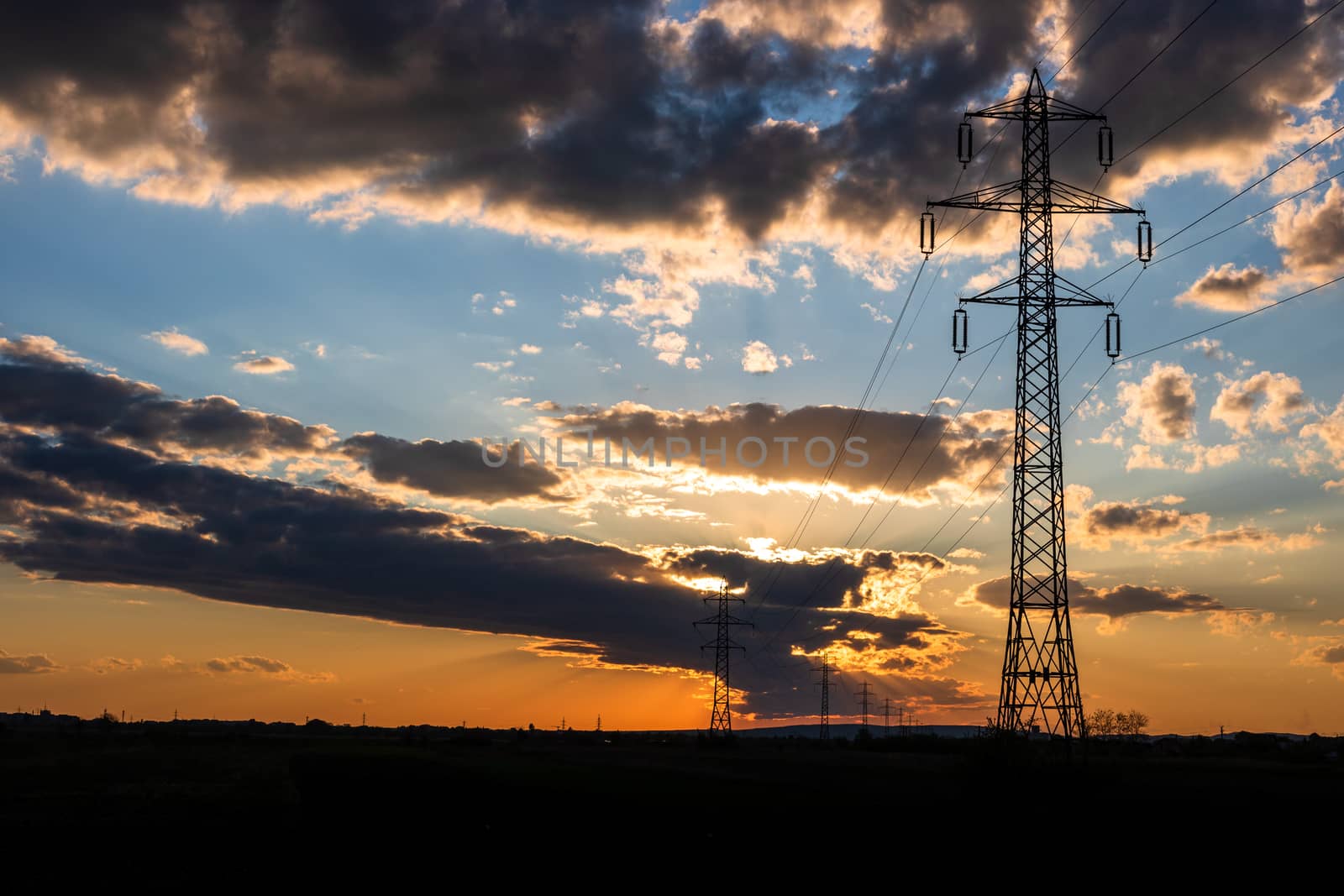 Beautiful dramatic sky and clouds, sunset lights over the transmission tower (electricity pylon) on a field.