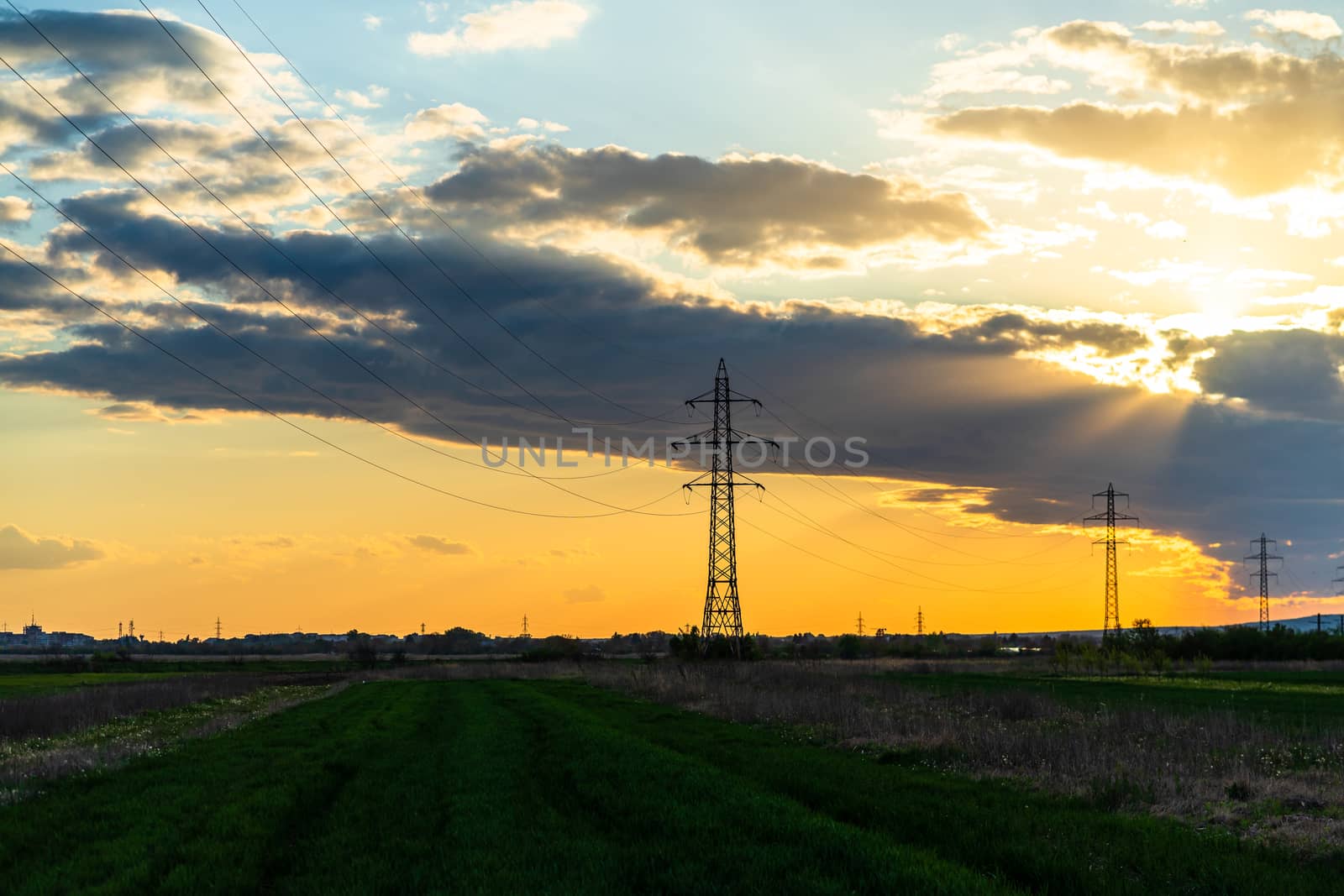 Beautiful dramatic sky and clouds, sunset lights over the transmission tower (electricity pylon) on a field.