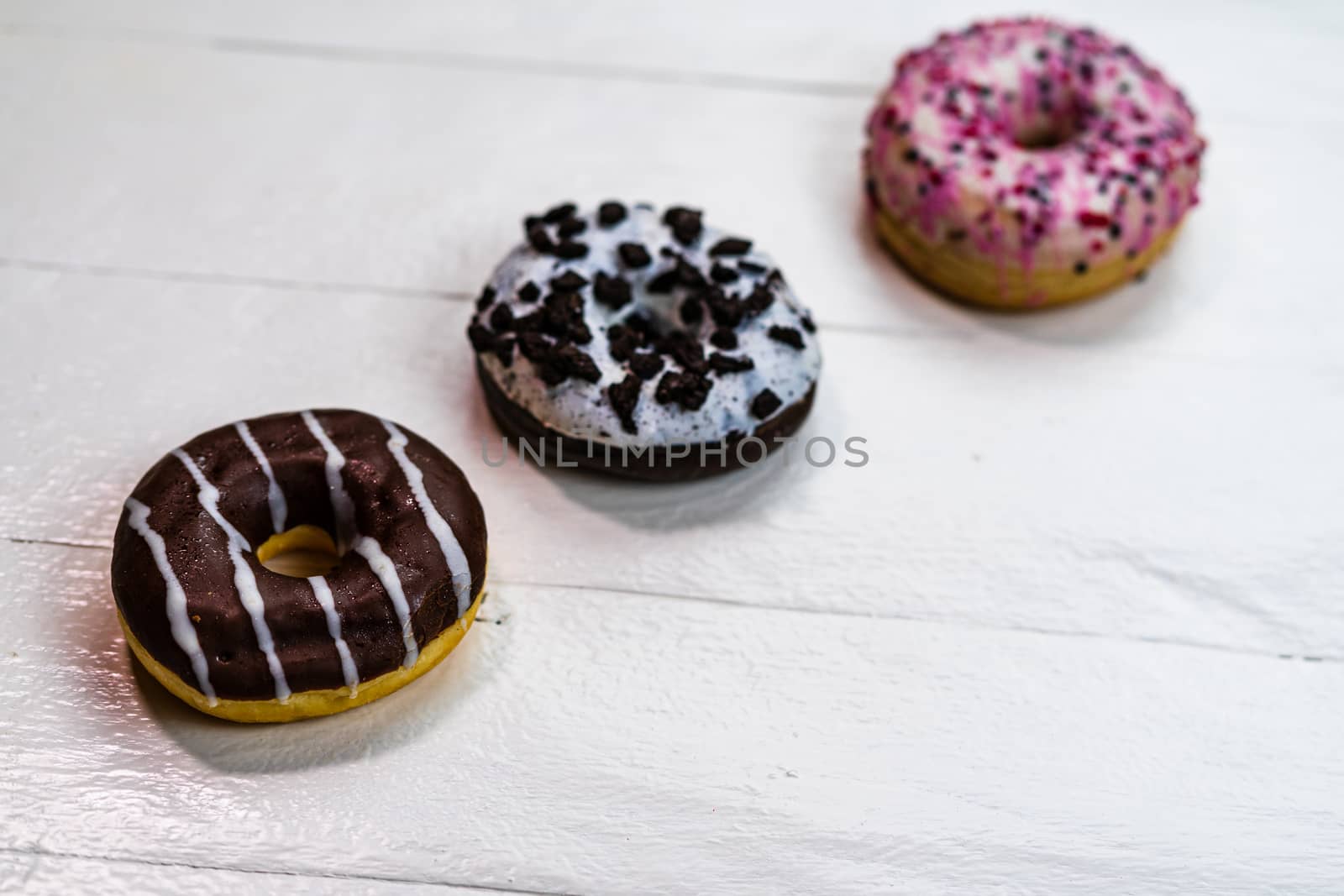 Colorful donuts on white wooden table. Sweet icing sugar food with glazed sprinkles, doughnut with frosting. Top view with copy space