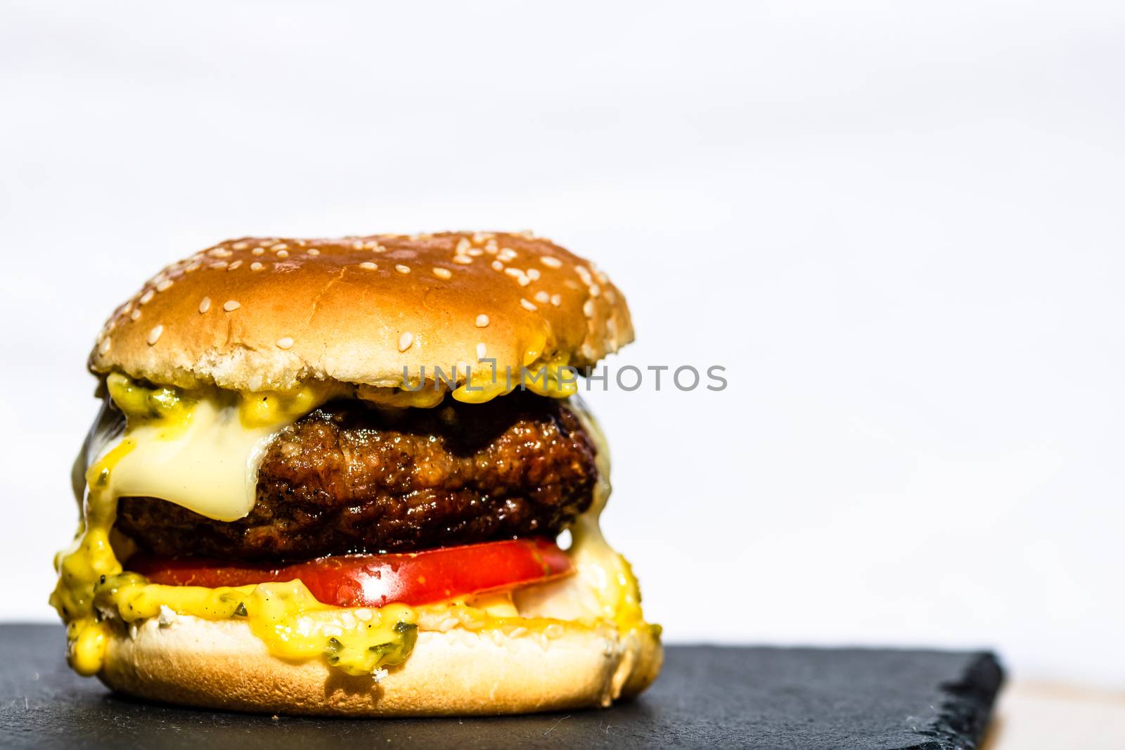 Detail of tasty beef cheeseburger isolated on white background. Cheeseburger with pickles, tomatoes, onion, melting cheese.