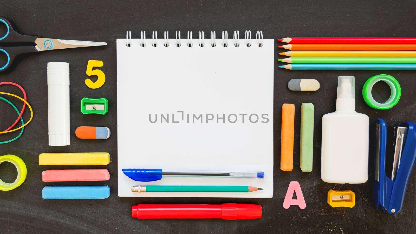 Top view on colorful stationery. Back to school flat lay concept. Horizontal 16:9 blackboard background with copy space on notepad.