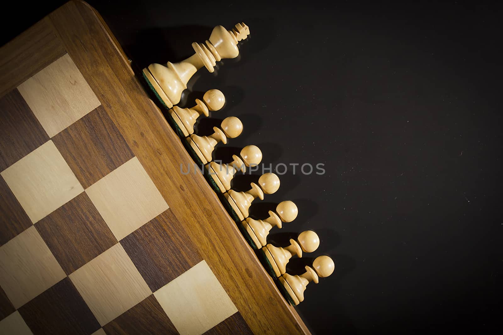 Wooden chess pieces and chess board on black background