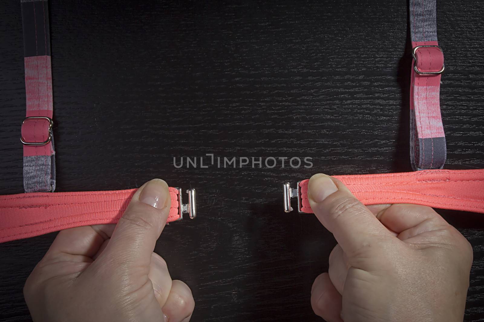 Female hands buttoning a swimsuit on a black background