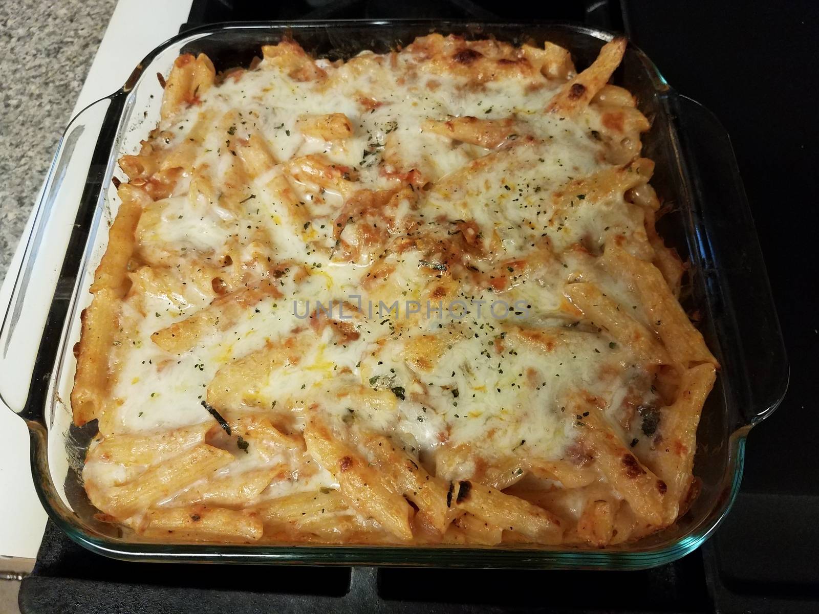 baked cheesy penne pasta in glass container on stove by stockphotofan1