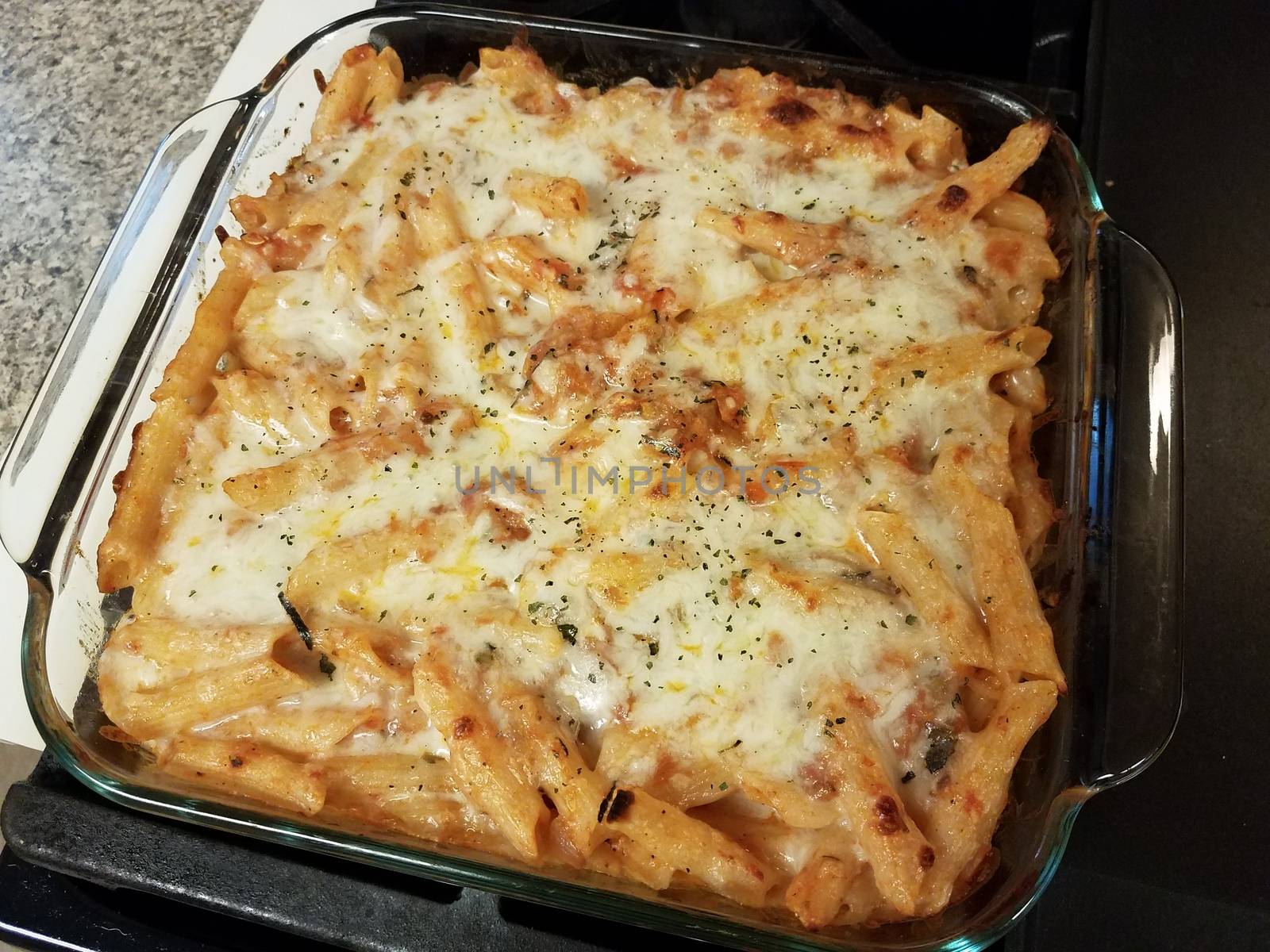 baked hot cheesy penne pasta in glass container on stove