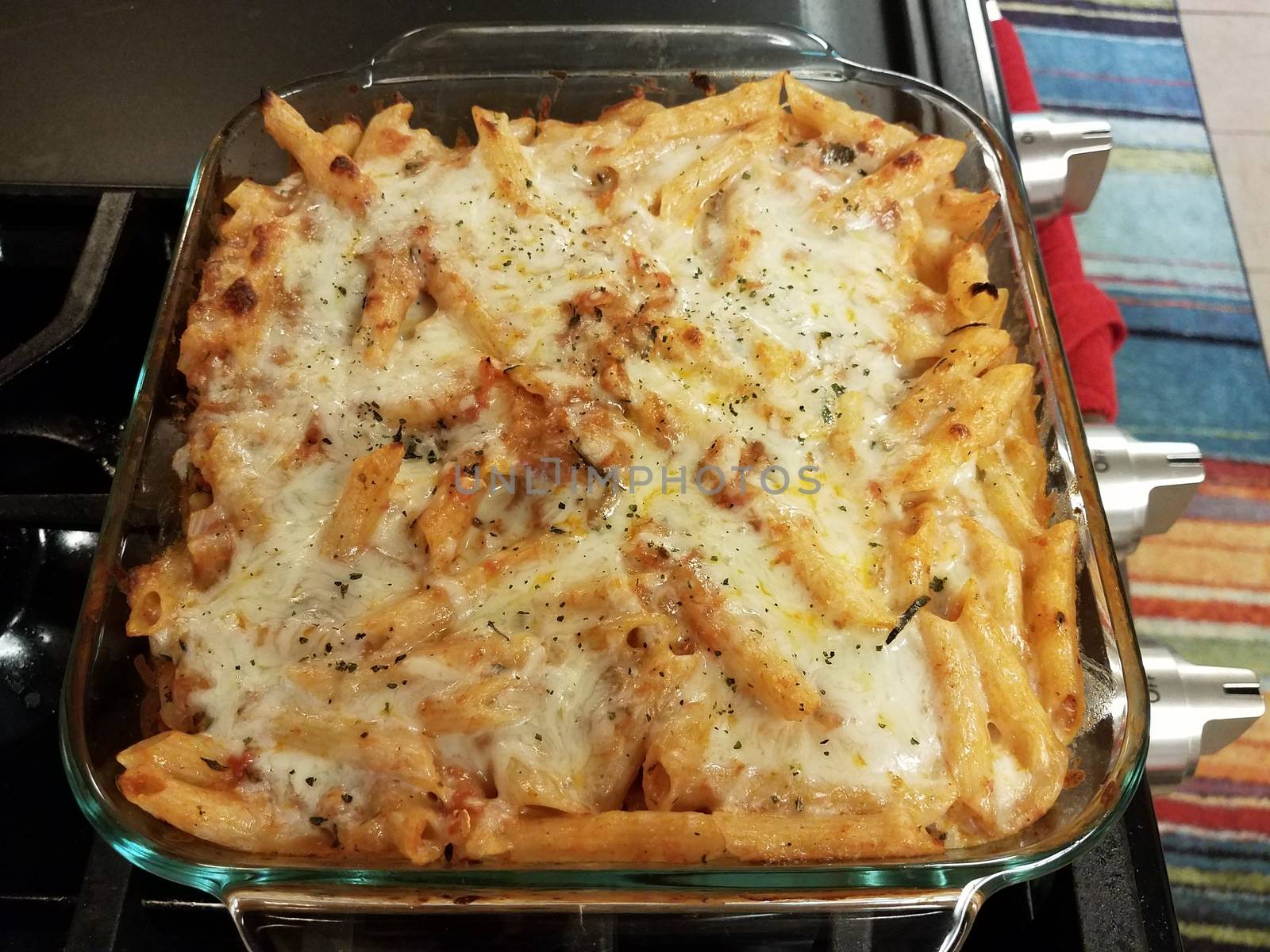 baked hot cheesy penne pasta in glass container on stove