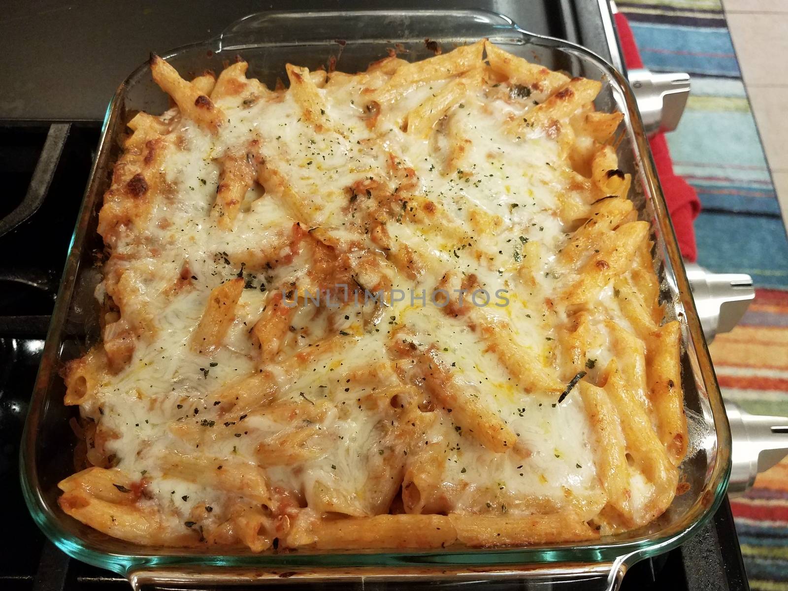 baked cheesy penne pasta in glass container on stove by stockphotofan1