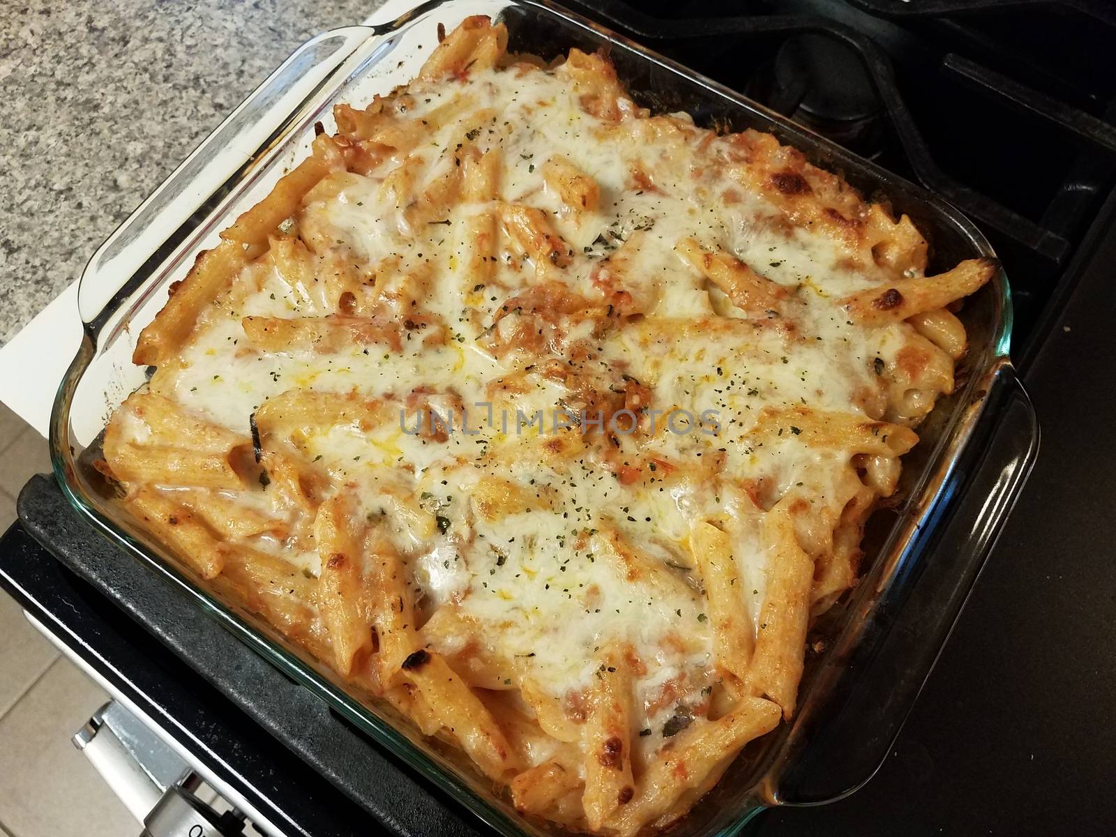 baked cheesy penne pasta in glass container on stove by stockphotofan1