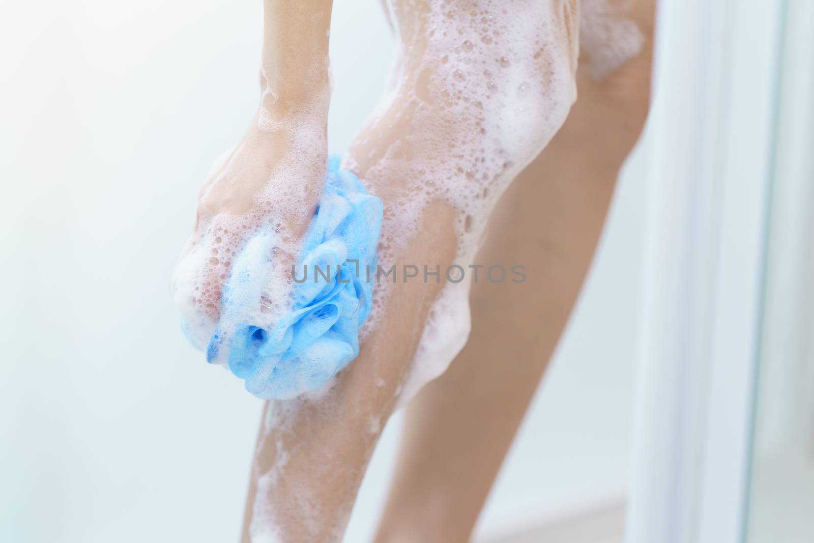 Woman washing her leg with bath sponge.