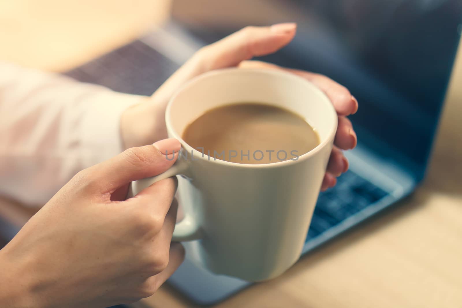 Woman hand on work desk with a laptop computer, a cup of coffee, with morning sunlight.