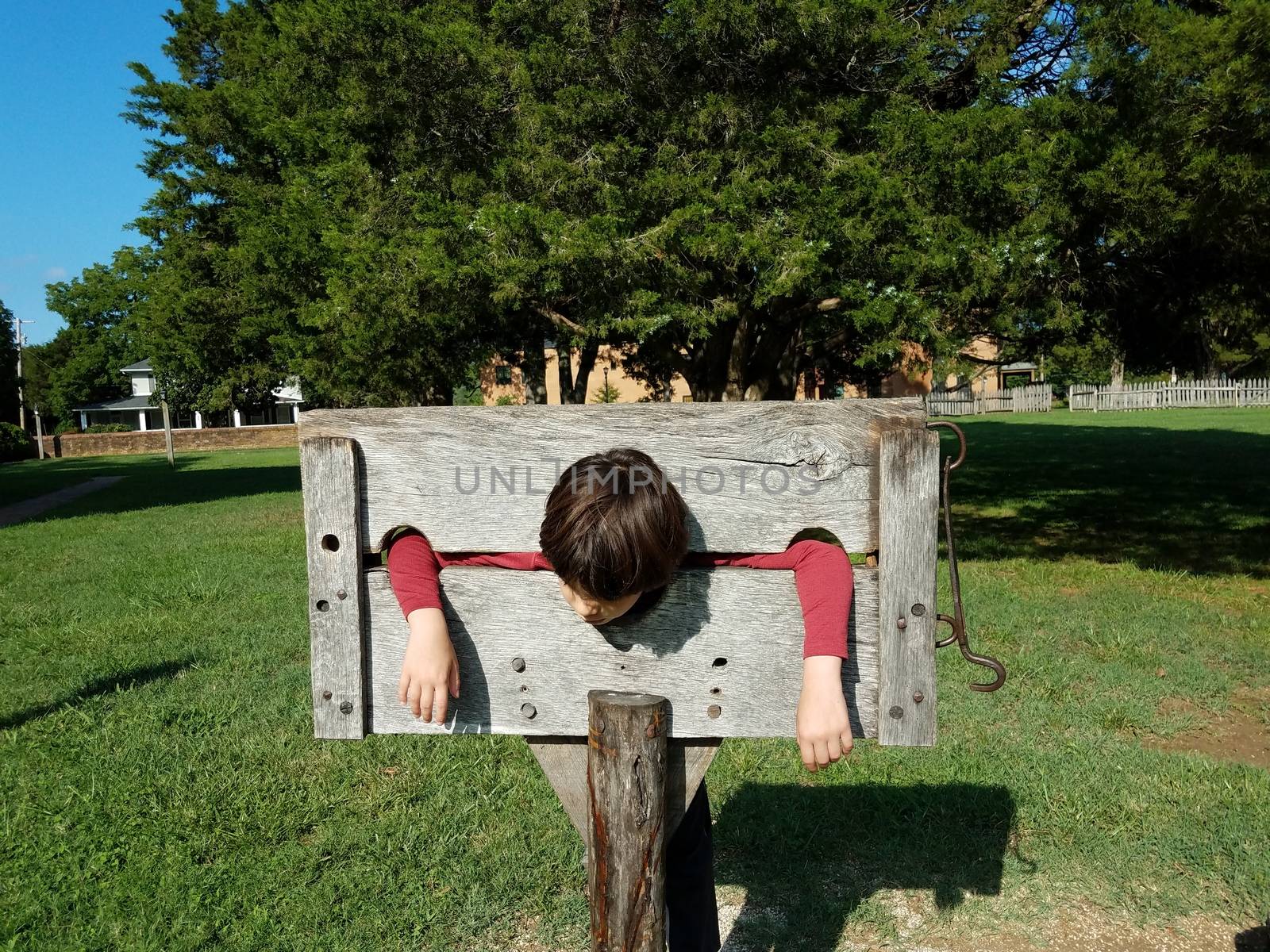 child playing in wooden stock punishment device and grass or field