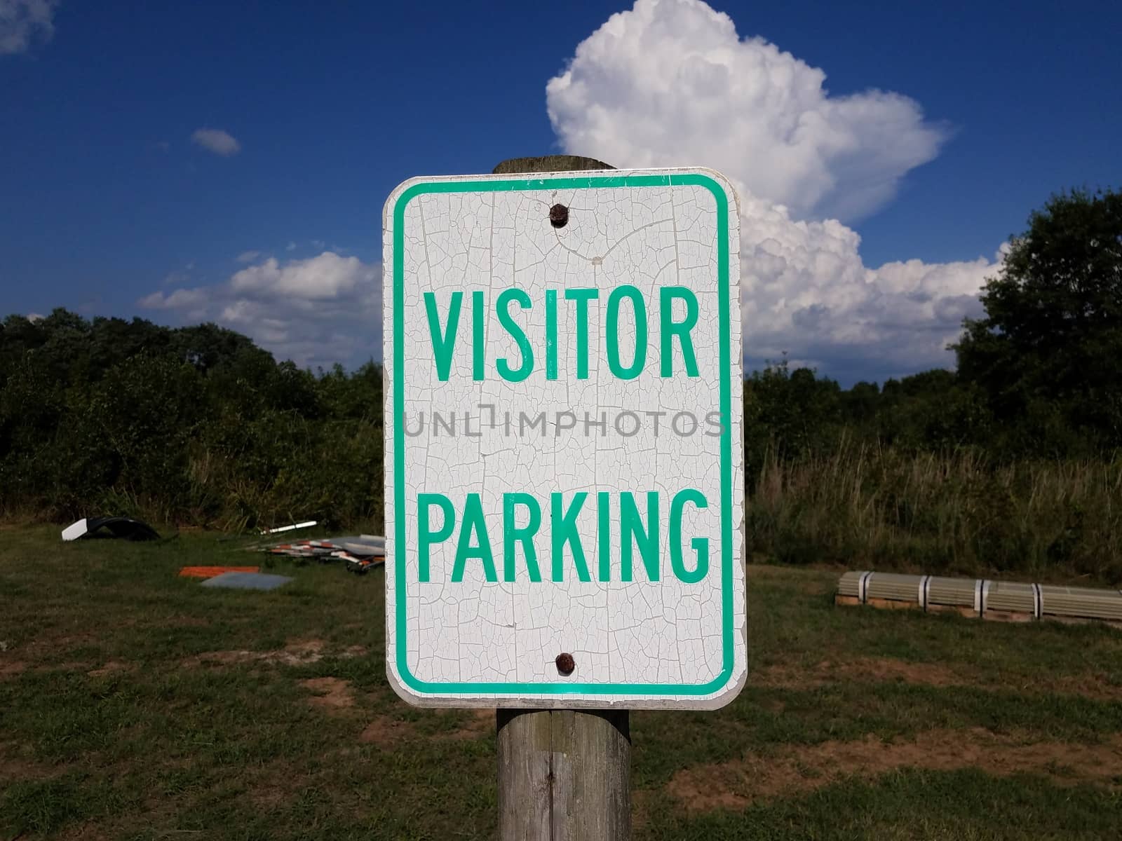 weathered white and green visitor parking sign and grass