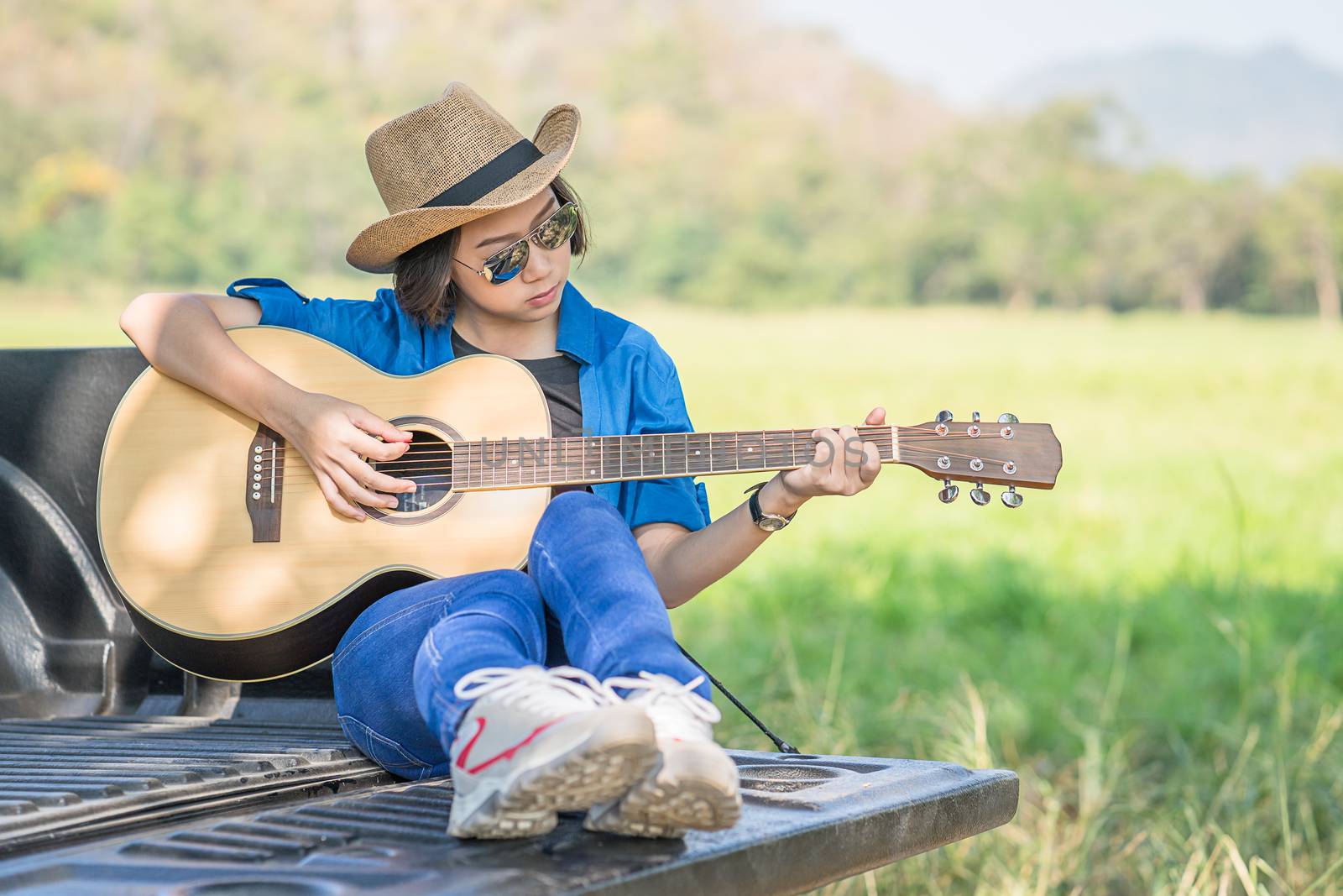 Woman wear hat and playing guitar on pickup truck by stoonn