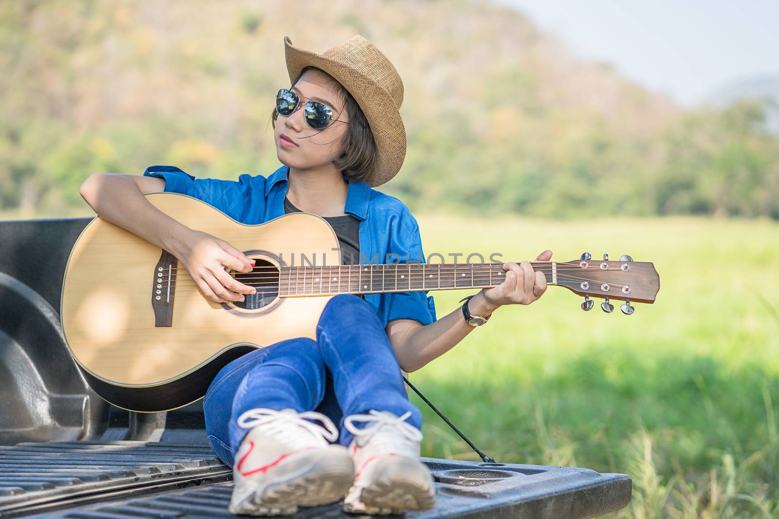 Woman wear hat and playing guitar on pickup truck by stoonn