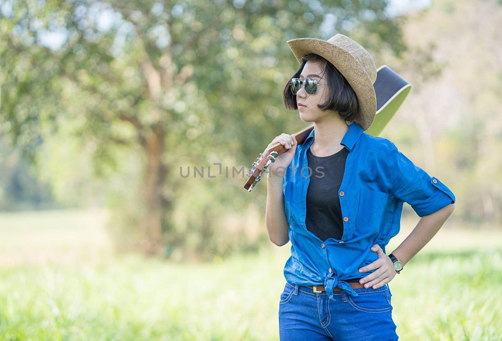 Woman wear hat and carry her guitar in grass field  by stoonn