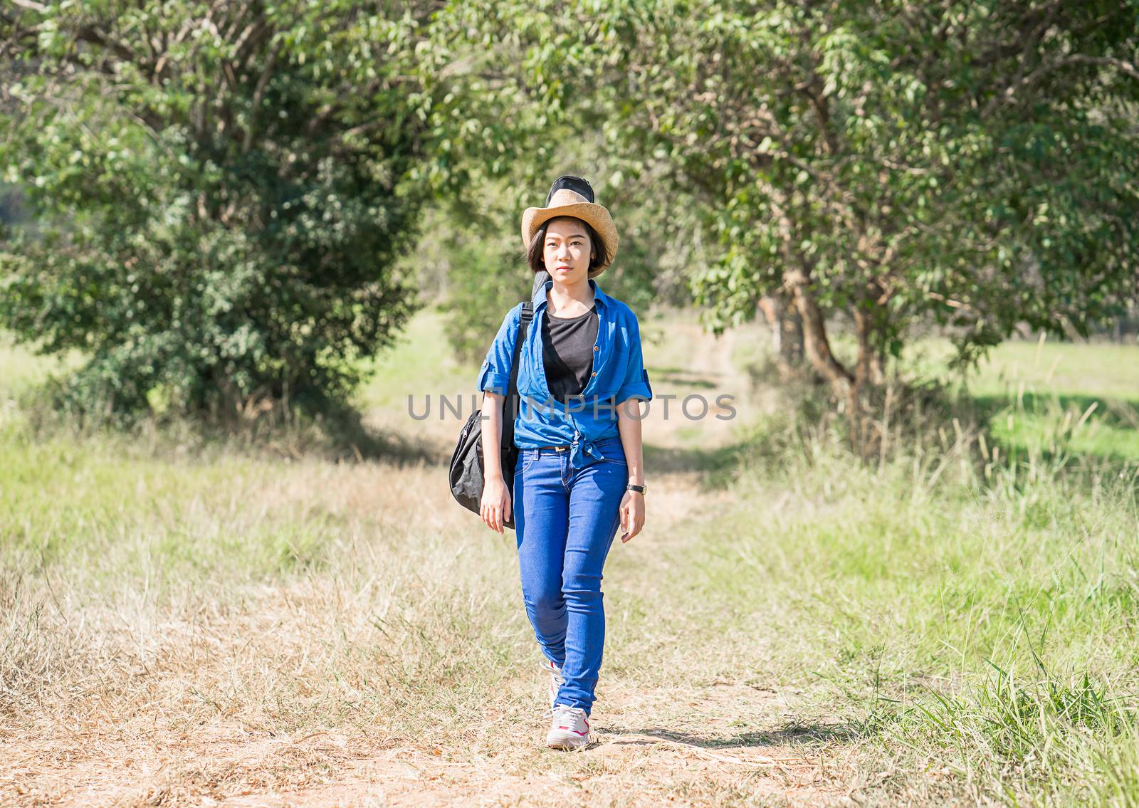 Young asian woman short hair wear hat walking and carry her guitar bag along in countryside Thailand