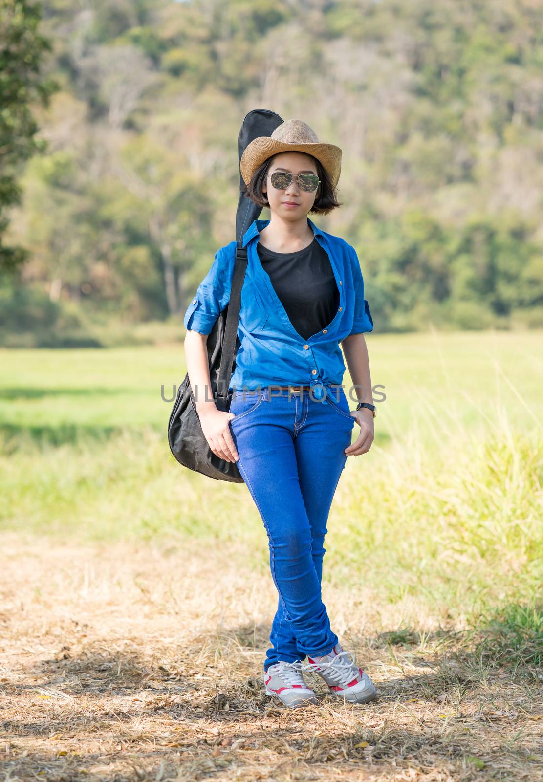 Young asian woman short hair wear hat walking and carry her guitar bag along in countryside Thailand